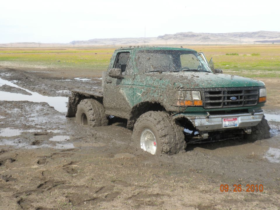 Green pickup truck stuck deep in mud, front end visible