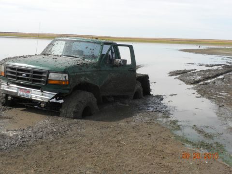 1989 Ford Bronco - A green Ford truck is stuck in the mud near a body of water.