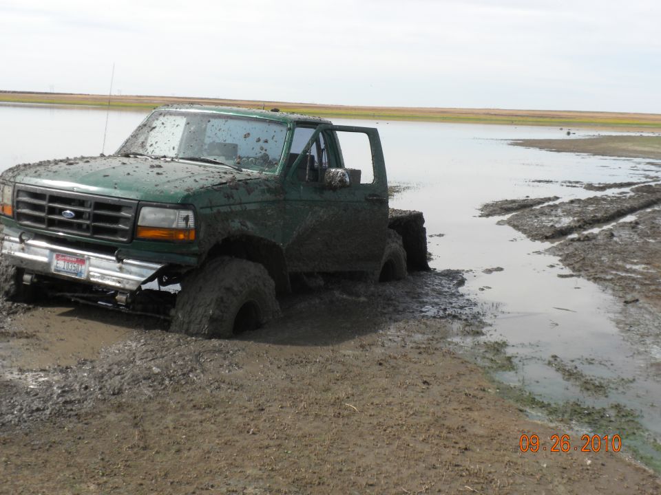 Green Ford truck stuck in mud, front driver side wheel submerged, door open
