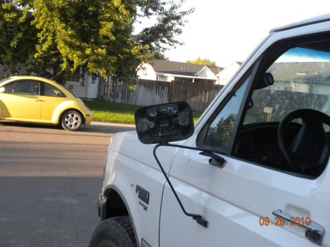 1989 Ford Bronco - White pickup truck and yellow VW Beetle parked on a street with houses in the background.