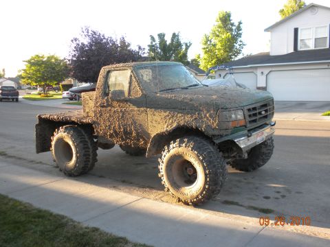1989 Ford Bronco - This heavily muddied flatbed truck is parked on a residential street, its large tires hinting at off-road use.