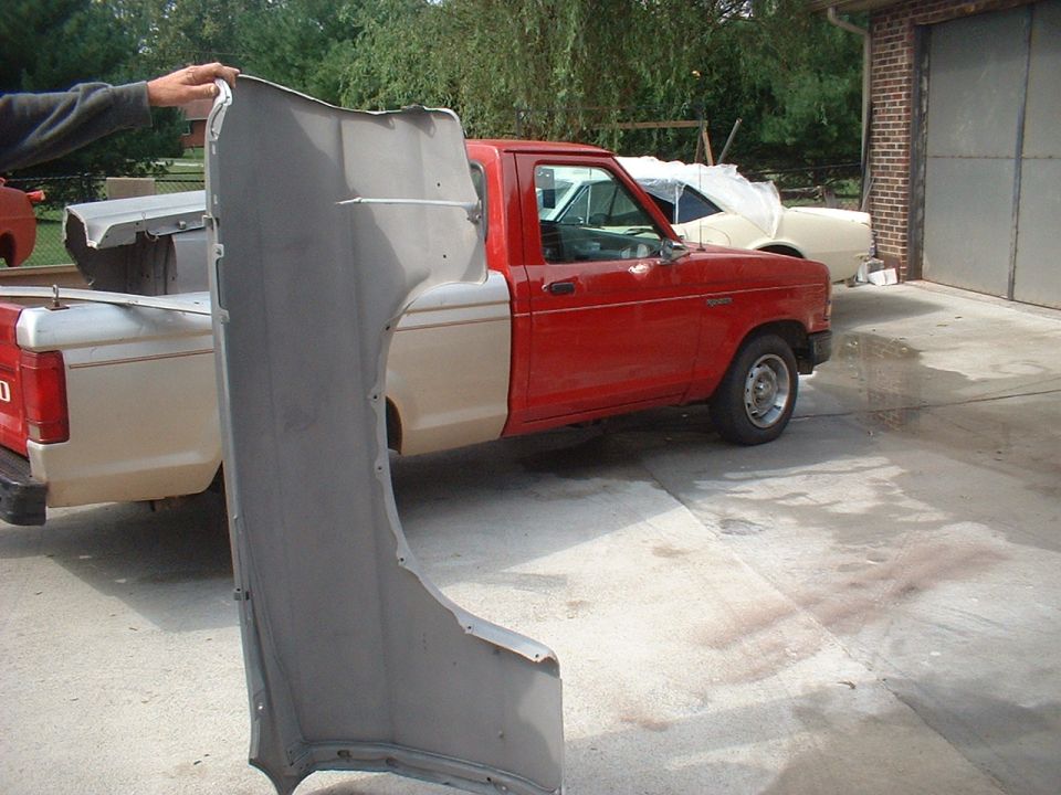 Red pickup truck with a beige bed, held gray fender in foreground