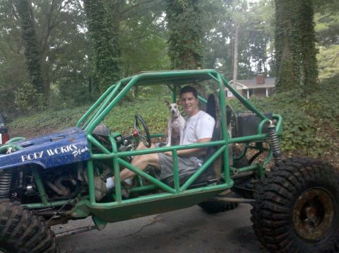 1994 Ford Bronco - A man and his dog sit in a custom-built buggy with a prominent roll cage and off-road tires.