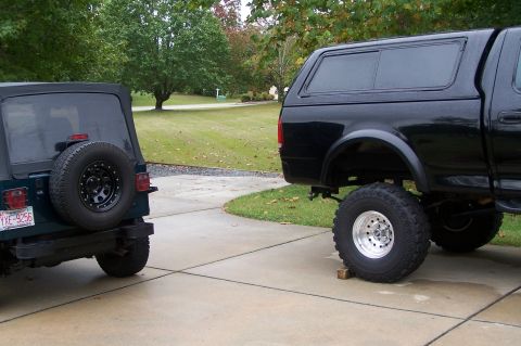 2000 Ford F-150 - A black 2000 Ford F-150 pickup truck with a camper shell and lifted suspension is parked next to a dark green Jeep.