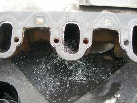 1984 Ford Bronco - Debris is visible on the gasket surface of an engine intake manifold, suggesting it is being worked on.