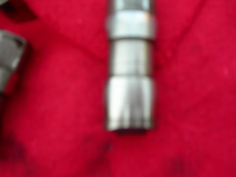 Metal engine component with stacked sections on red fabric, with a Supermotors.net watermark