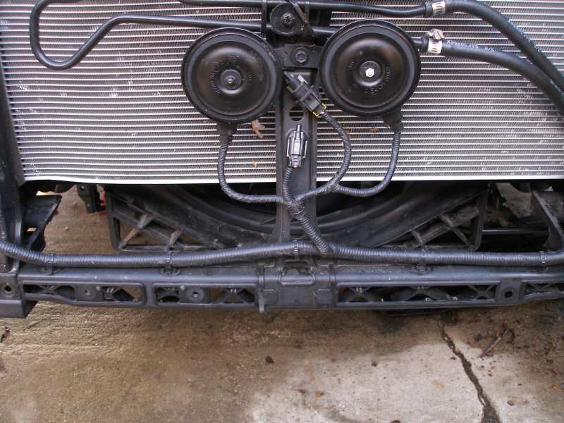 Car horns mounted in front of a radiator with black plastic bracing