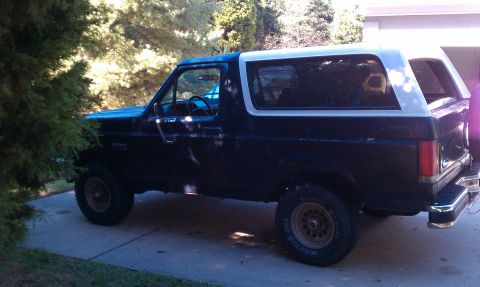 1987 Ford Bronco - This Ford Bronco is parked in a driveway next to some trees.