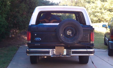 1987 Ford Bronco - Rear view of a black Ford Bronco with a white top and a spare tire on the back.