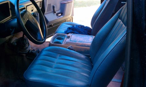 1987 Ford Bronco - The interior of this vehicle shows blue seats, a center console with cup holders, and a steering wheel.