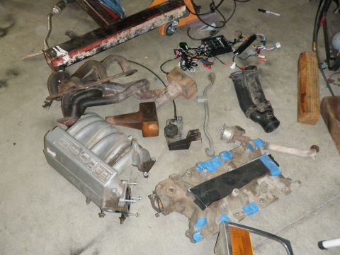 1994 Ford Bronco - Various engine parts, including an intake manifold marked "5.0", are laid out on a concrete surface.