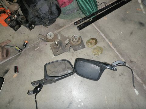 1994 Ford Bronco - Two side mirrors and engine mounts are laid out on a concrete surface, possibly for sale or repair.