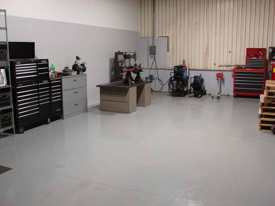 Workshop interior with tool chests, a drill press, welding equipment, and stacked pallets