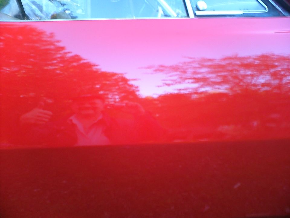 Red vehicle door with reflection of man giving thumbs up. Supermotors.net logo visible