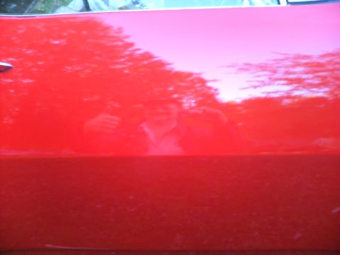 1989 Ford Bronco - Reflection of trees and a person in a shiny red car door.
