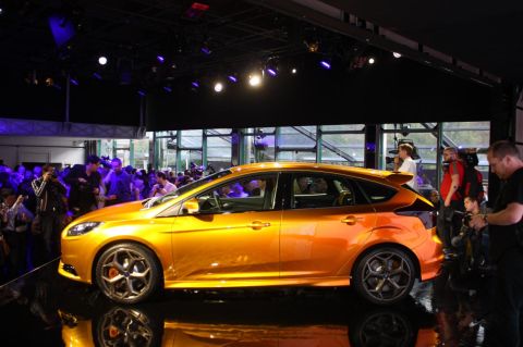 1993 Ford Taurus - An orange hatchback car is displayed on a reflective surface with an audience in the background.