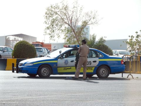 1999 Mercury Grand Marquis - A police officer stands next to a blue and white patrol car with Arabic text and 'TRAFFIC' visible on the side.
