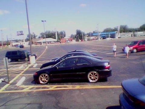 1999 Ford Taurus - Side view of a black Honda Civic coupe with gold/bronze multi-spoke wheels parked in a sunlit parking lot, with a second dark coupe lined u…