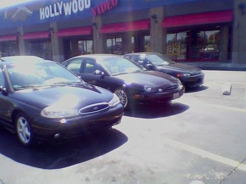 1999 Ford Taurus - Three sedans are parked in front of a Hollywood Video store.