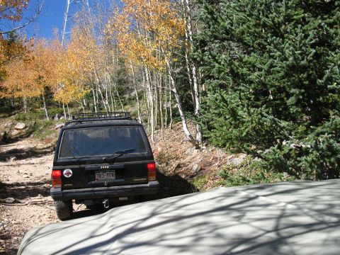 1978 Ford Bronco - A black Jeep Cherokee navigates a dirt road surrounded by autumn trees.