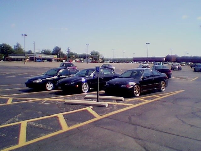 Several dark-colored cars parked in a lot on a sunny day