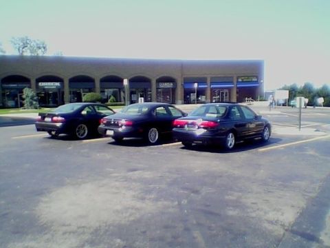 1999 Ford Taurus - Three 1999 Ford Tauruses are parked in a lot outside a commercial building.