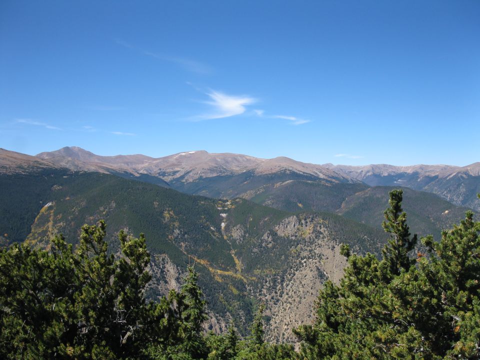Mountain range under a blue sky with scattered clouds, foreground pine trees