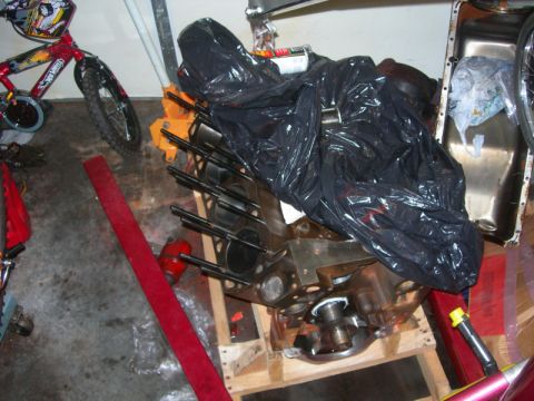 1984 Ford Bronco - An engine block is covered with a black trash bag and rests on a wooden pallet in a garage setting.