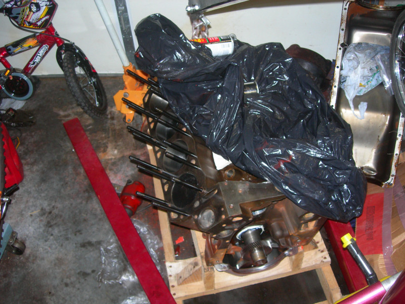 Engine block covered in a black trash bag, sitting on a wooden pallet. A red bicycle is to the left