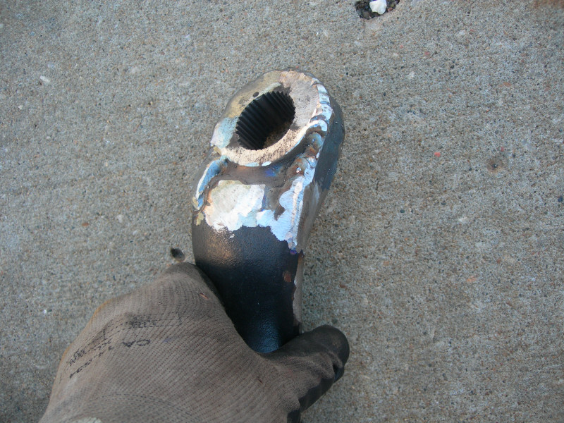 Gloved hand holding a dark metal part with visible welding and splines