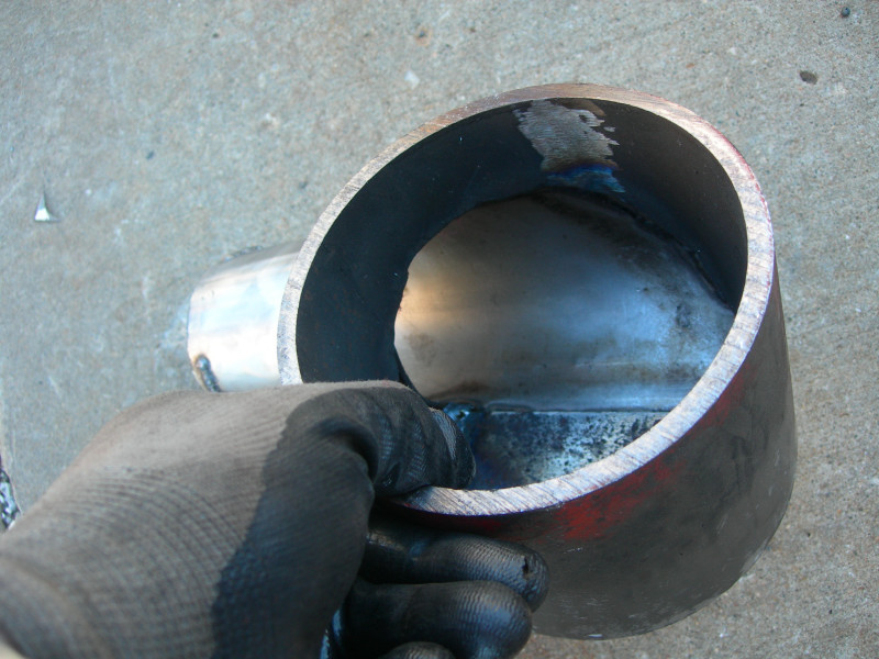 Gloved hand holding a section of metal exhaust pipe with visible welds inside