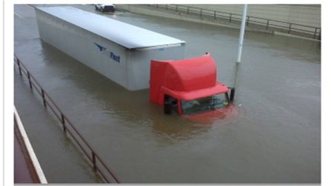 1972 Ford Ranchero - Elevated view of a red semi tractor with a white box trailer stranded in deep floodwater on a sunken roadway, water up to the cab windows a…