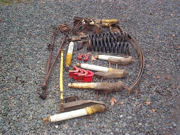 Assorted suspension parts including shocks, springs, and linkages on a gravel surface