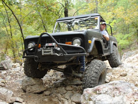 1967 Ford Mustang - A man drives a modified black Ford Bronco over a rocky terrain on an off-road trail.