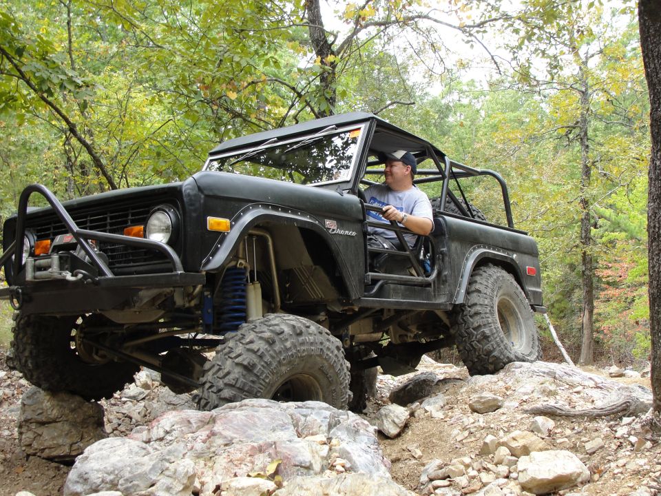 Black Ford Bronco with a roll cage and large tires navigating rocky terrain