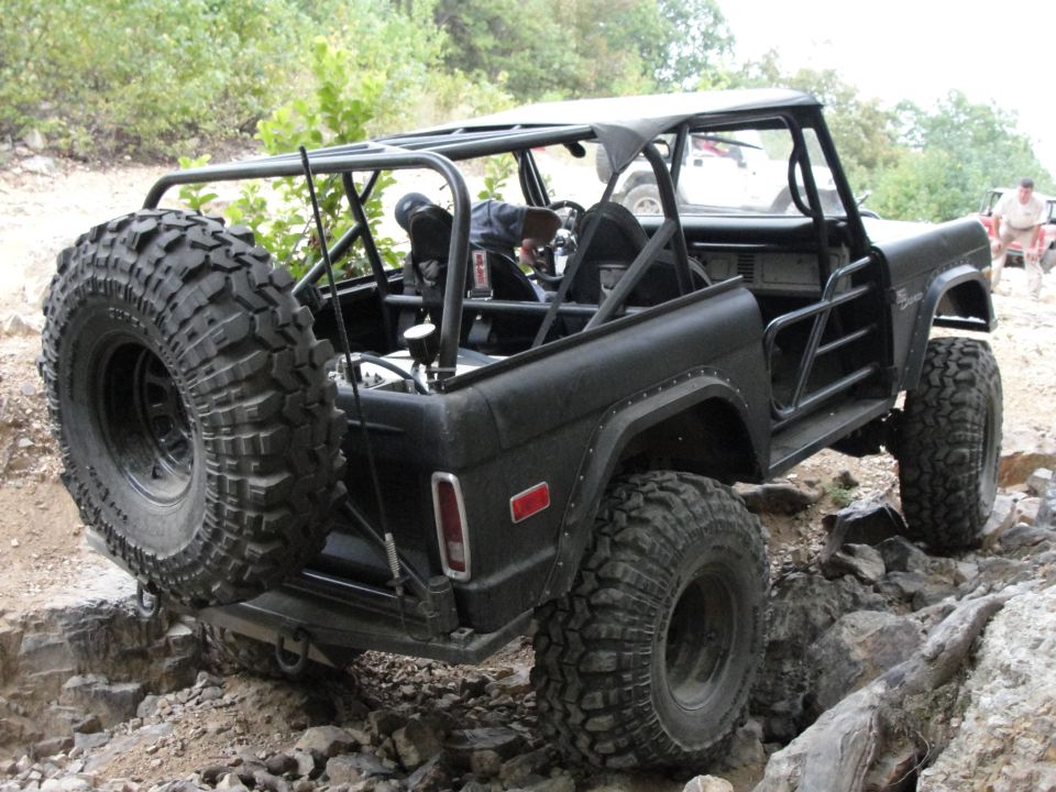 Black 1970s Ford Bronco with roll cage and large tires on rocky terrain