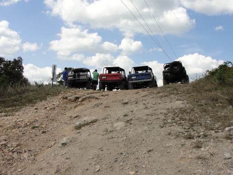 1967 Ford Mustang - Several off-road vehicles are lined up on a dusty incline, with a cloudy sky overhead and power lines overhead.