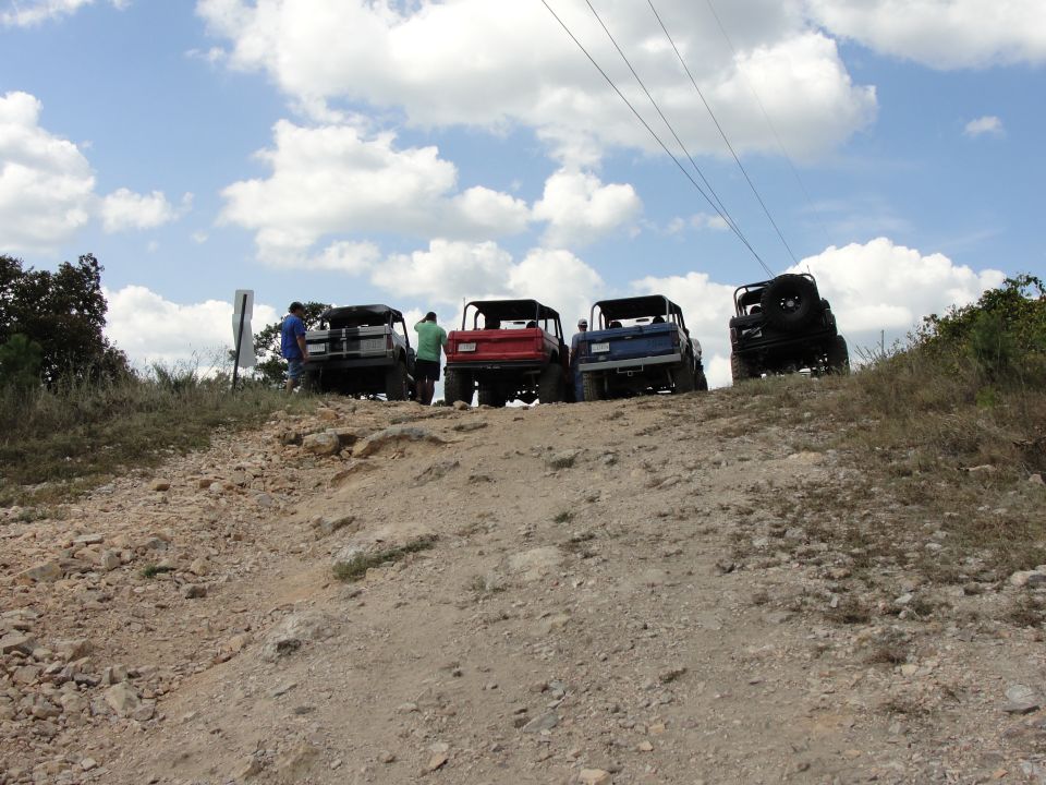 Four off-road vehicles parked on a dirt hill under a cloudy sky