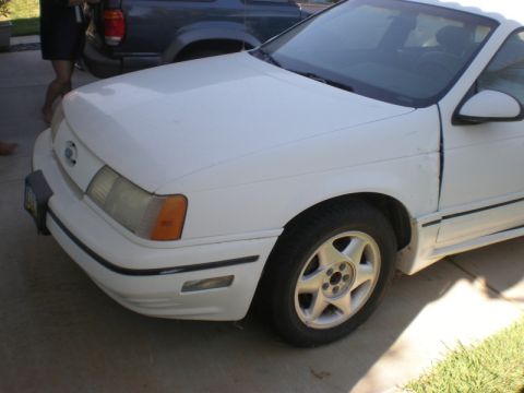 1990 Ford Taurus - A white 1990 Ford Taurus is parked in front of a dark SUV.