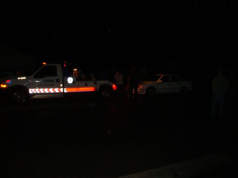 1990 Ford Taurus - A white sedan is being loaded onto a tow truck in the dark.