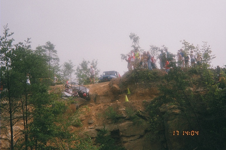 Distant rock buggy on eroded dirt hillside with spectators silhouetted on the crest