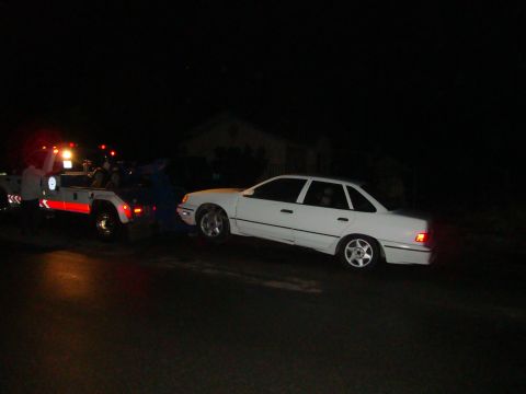 1990 Ford Taurus - A white sedan is being towed by a tow truck at night.