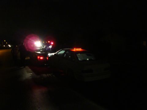 1990 Ford Taurus - A white 1990 Ford Taurus is being towed at night, with its hazard lights illuminated.