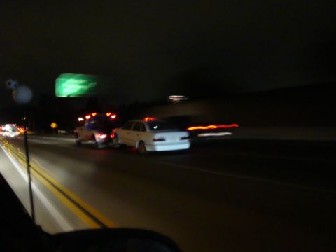 1990 Ford Taurus - A white sedan is seen from behind on a highway at night, with its taillights blurred by motion.