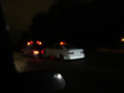 1990 Ford Taurus - Two white sedans with emergency lights are visible on a dark road at night.