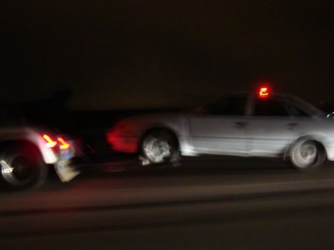 1990 Ford Taurus - A white sedan is being towed at night, with its red taillights illuminated.