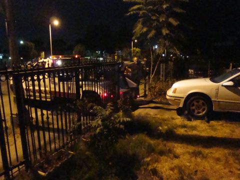 1990 Ford Taurus - A white sedan is parked on the side of the road at night, with a police car and several individuals in the background.