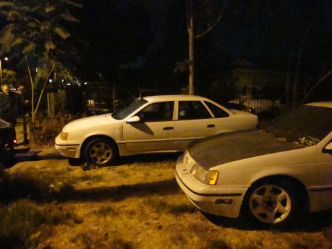 1990 Ford Taurus - Two white sedans are parked outdoors at night, with one partially obscuring the other.