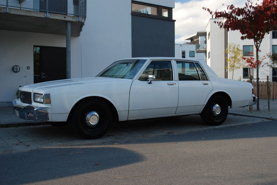 White 1980s sedan parked on street, side view