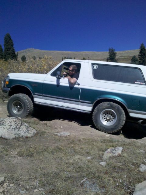 1996 Ford Bronco - 1996 Ford Bronco navigates a rocky off-road trail under a clear blue sky.